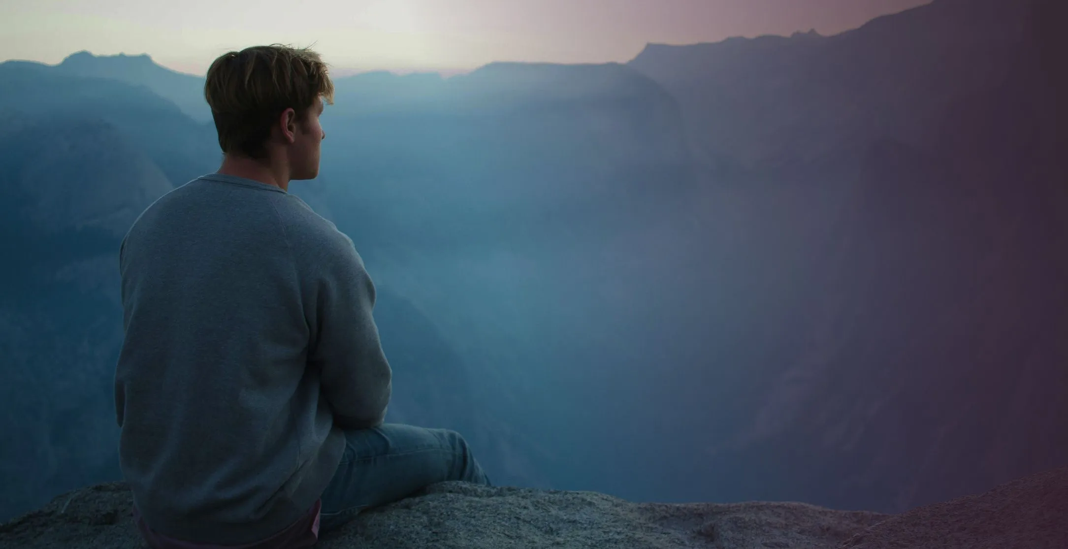 Mężczyzna siedzi na skale i patrzy na góry